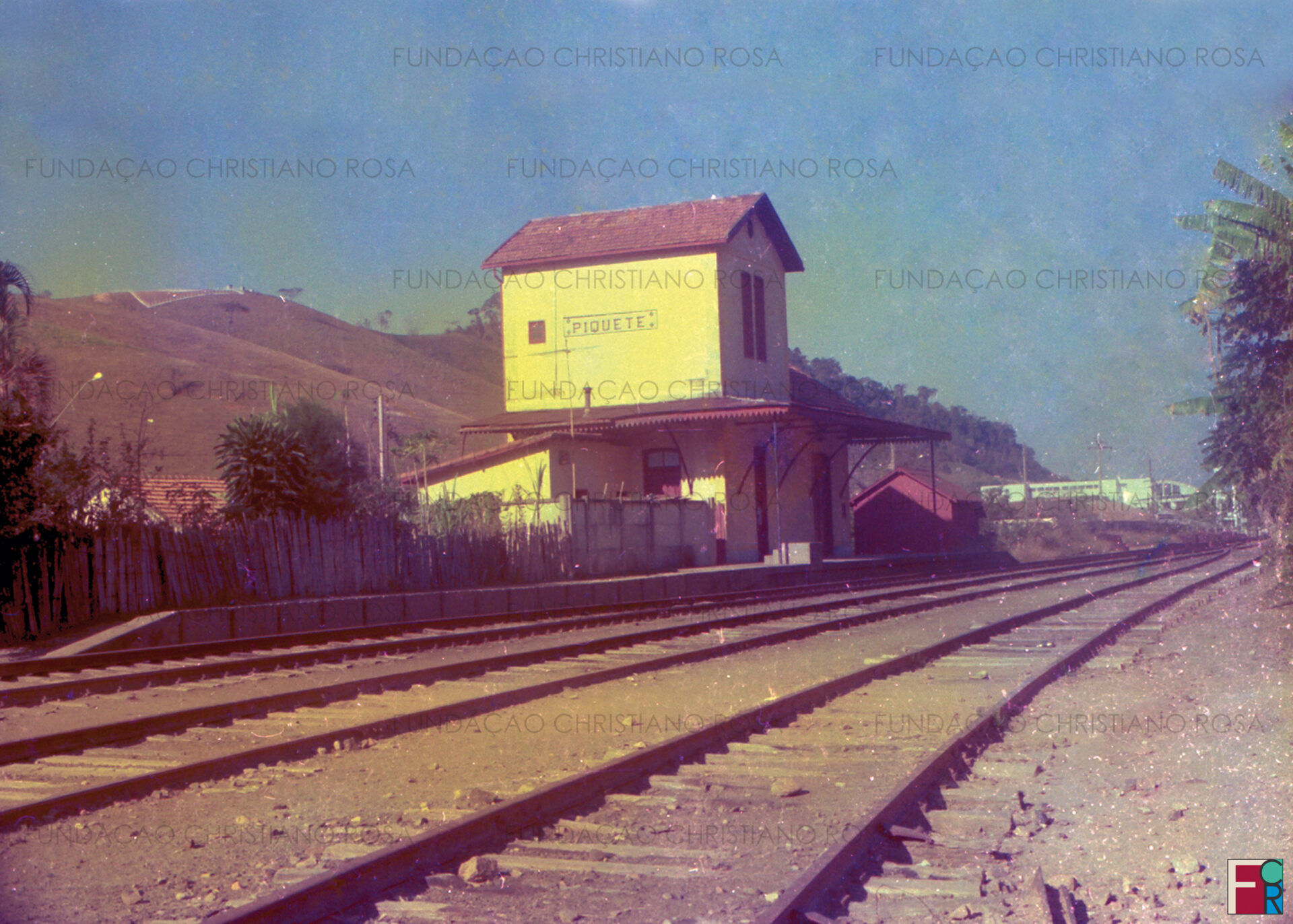 Trecho do ramal férreo Lorena x Piquete. Em primeiro plano a Estação Ferroviária Rodrigues Alves (Piquete) e, ao fundo, o Colégio Estadual Leonor Guimarães. Foto da década de 1970.