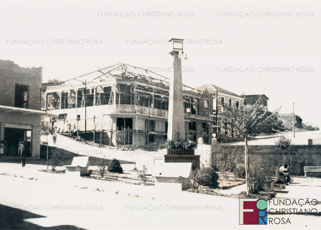 Praça da Bandeira em meados da década de 1940, com seu traçado original, que contava com o obelisco e o paredão junto ao pórtico de entrada da Vila Duque de Caxias. À Rua Cel. Luiz Relvas, obras dos prédios da Associação Comercial e da residência e casa comercial de Thomé Seraphim, a residência e loja de Elias Hankis e, ao alto, a casa da família de Benedito Chaves.